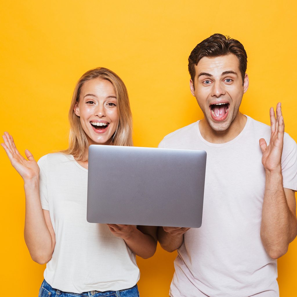 Happy young couple celebrating success while holding a laptop against a bright yellow background, representing effective online marketing strategies.