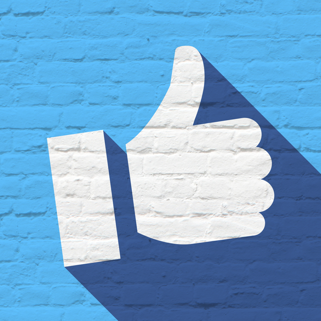 Thumbs up icon on a blue brick wall, symbolizing social media engagement and approval, relevant to Facebook marketing strategies.